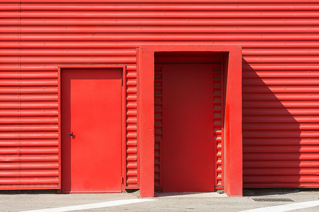 A striking image of a red corrugated metal building featuring two red doors, perfect for modern architecture projects.