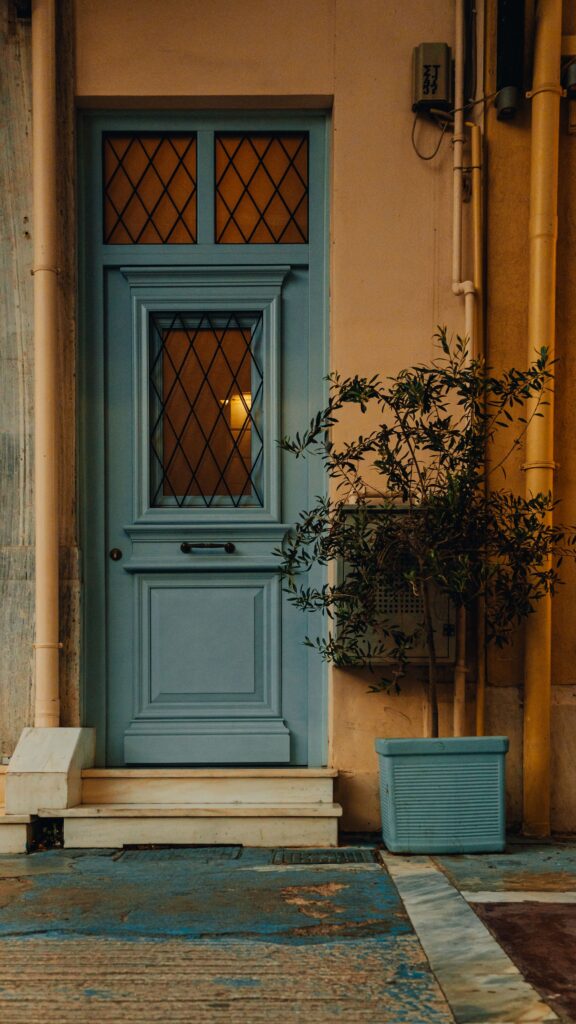 A quaint blue door with Mediterranean charm, framed by an olive plant in Athens, Greece.